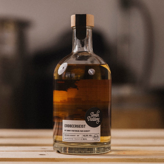 Eine Flasche Berlin Distillery Erdbeergeist steht auf einer Holzpalette vor dem Hintergrund der Produktionseinrichtung.