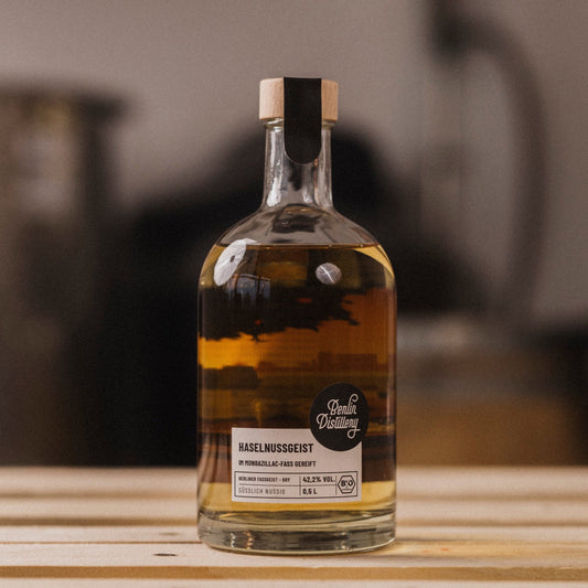 Eine Flasche Berlin Distillery Haselnuss Fassgeist steht auf einer Holzpalette vor dem Hintergrund der Produktionseinrichtung.