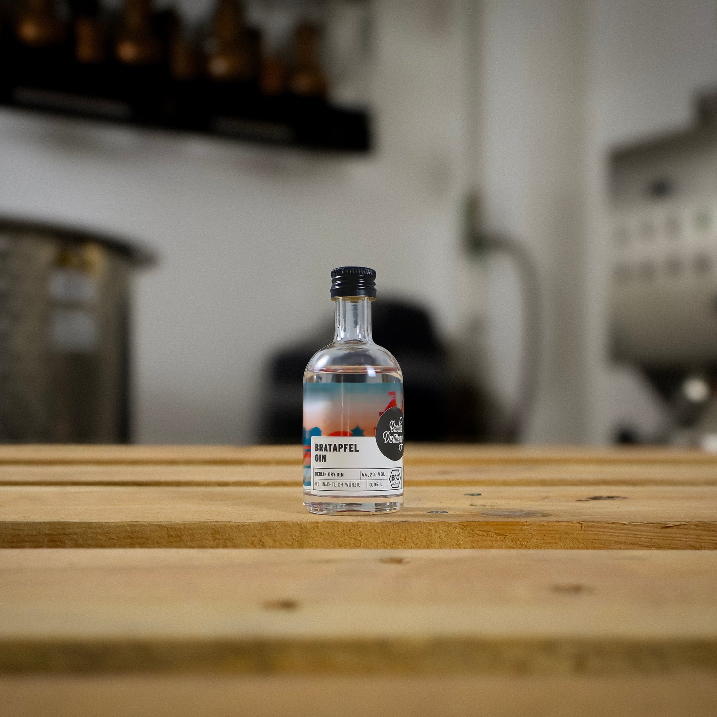 Eine kleine Flasche Berlin Distillery Bratapfel Gin steht auf einer Holzpalette vor der Produktionsanlage.